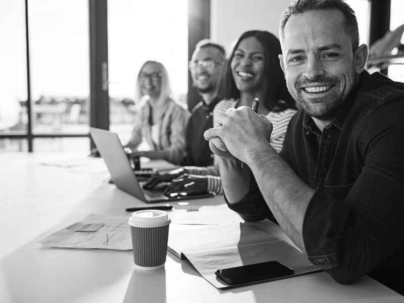 Das Webdesign Team sitzt an einem Tisch und lächelt in die Kamera.