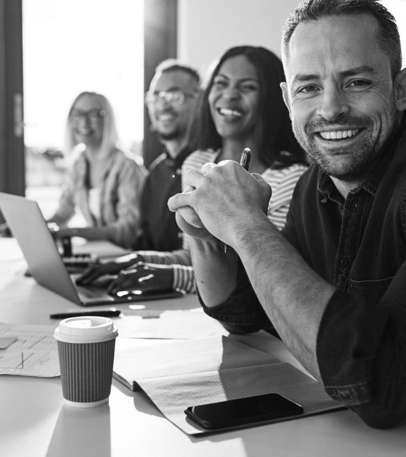 Das Webdesign Team sitzt an einem Tisch und lächelt in die Kamera.
