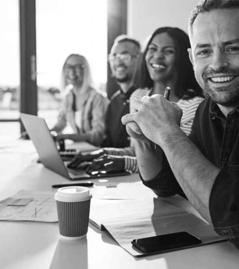 Das Webdesign Team sitzt an einem Tisch und lächelt in die Kamera.